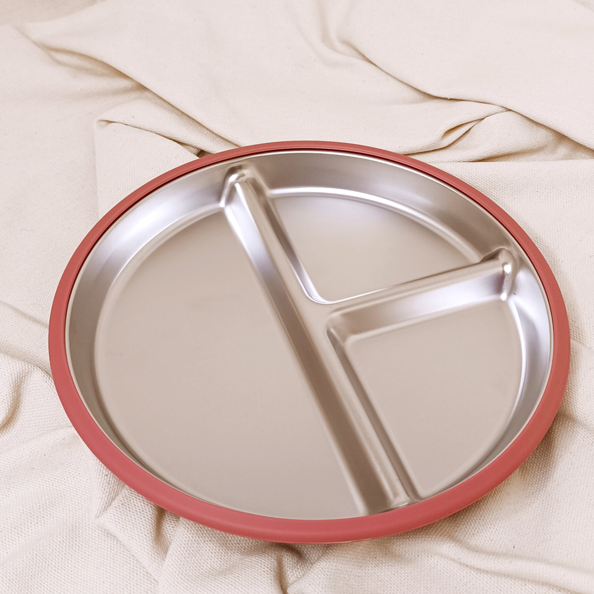 Stainless steel divided plate with pink rim on a beige fabric background