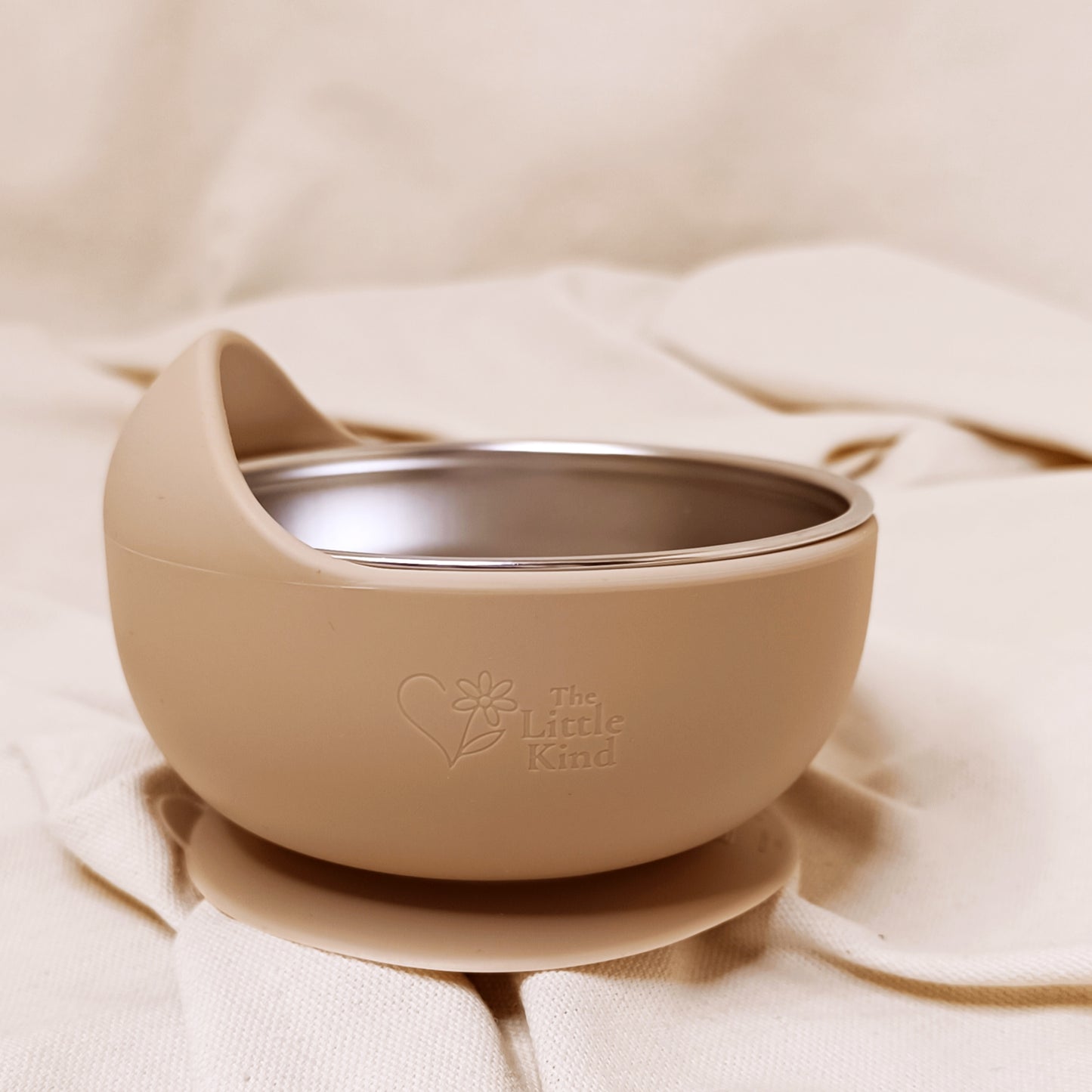 Beige bowl with a suction cup on a beige fabric background, featuring 'The Little Kind' logo.