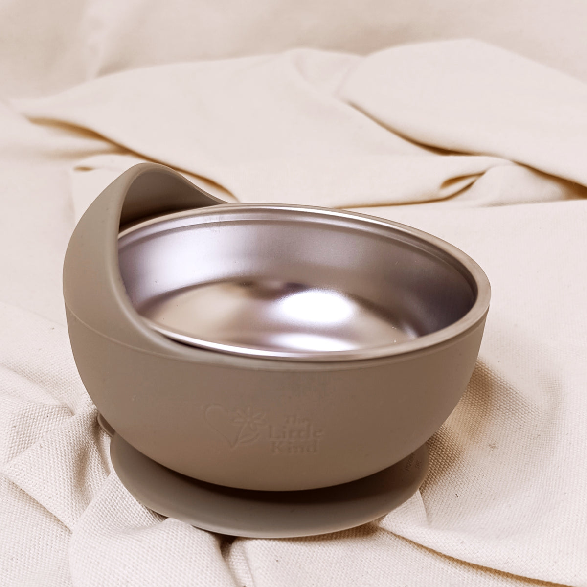 Olive baby bowl with a stainless steel interior on a beige fabric background