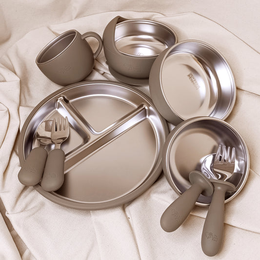 Children's stainless steel and Silicone dinnerware set with olive cups, plates, and cutlery on a white fabric background.