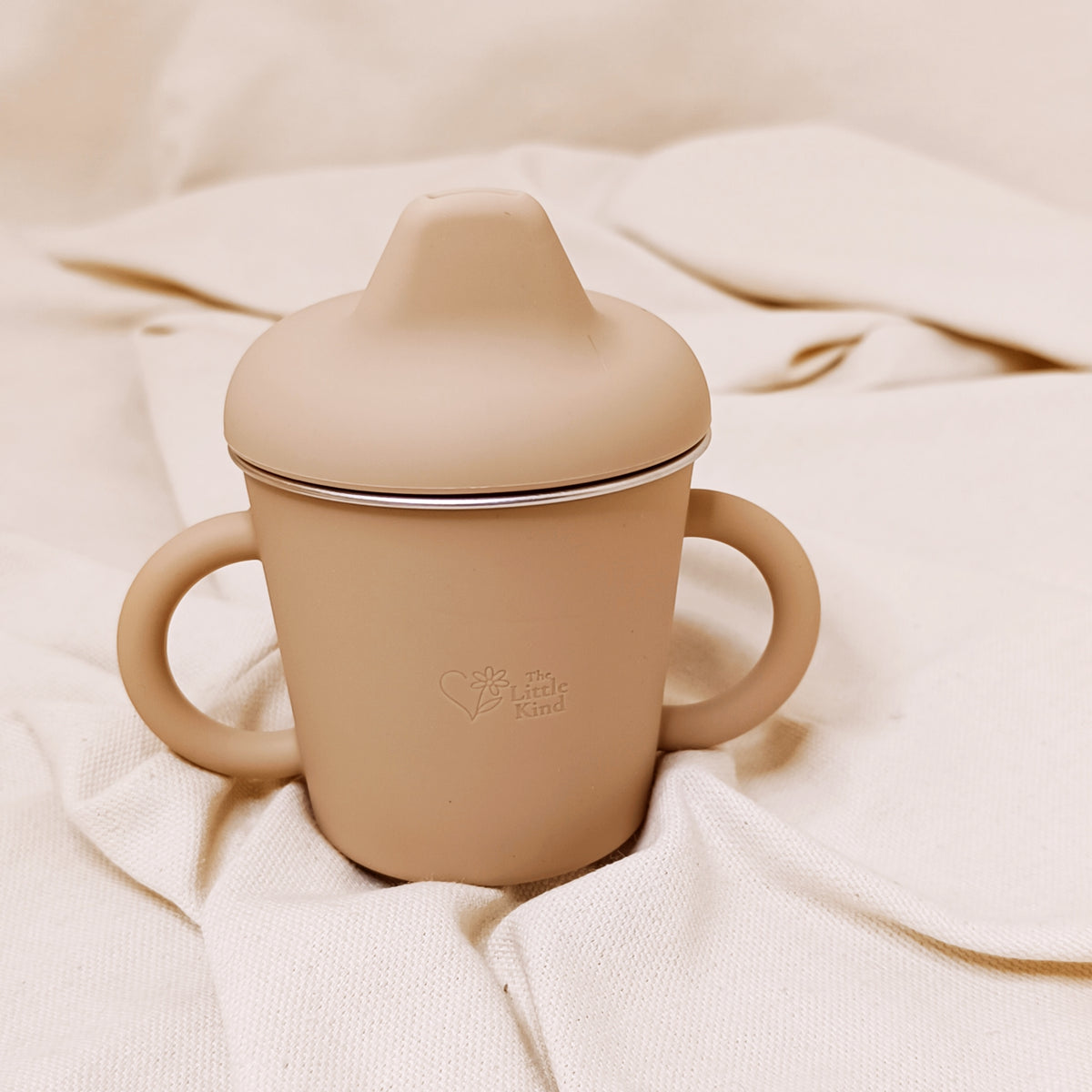 Beige sippy cup with a lid on a soft beige fabric background