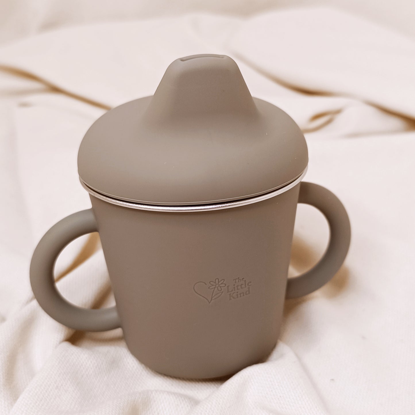 Olive sippy cup with lid on a soft beige fabric background