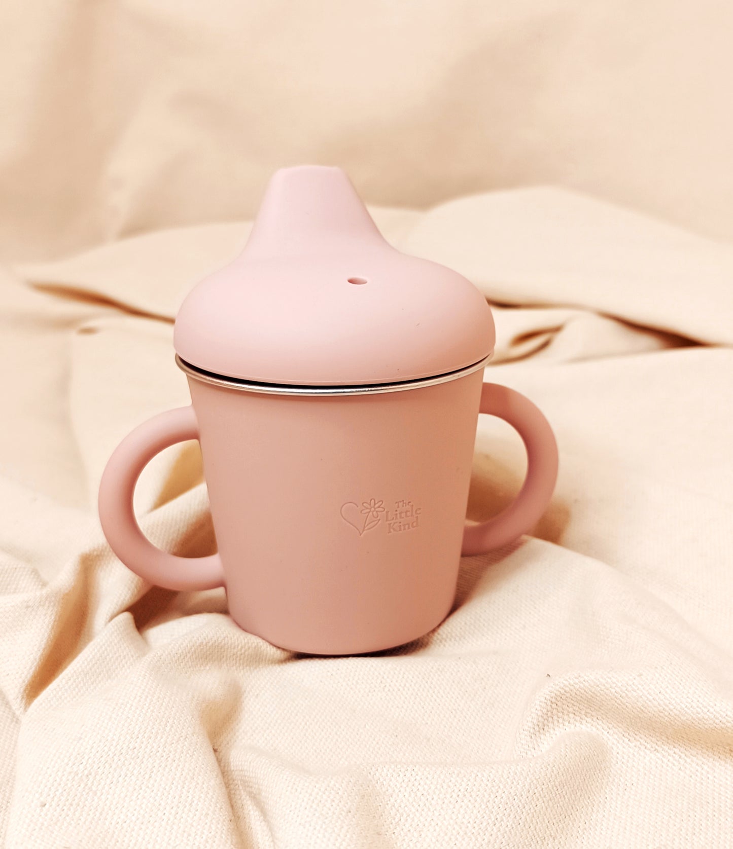 Pink sippy cup with a lid on a beige fabric background