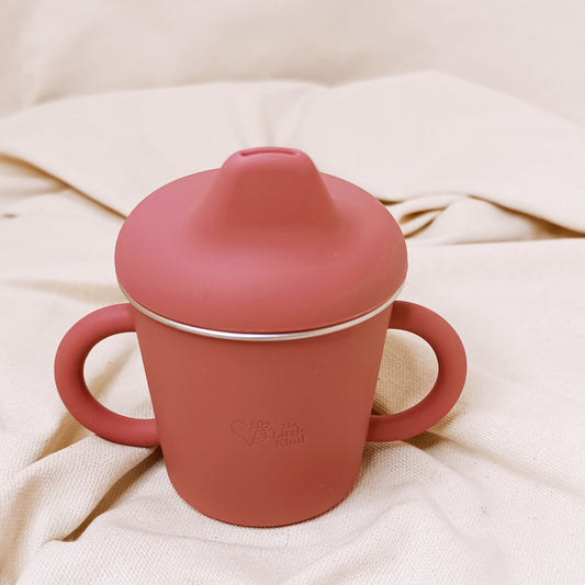 Pink sippy cup with a lid on a beige fabric background