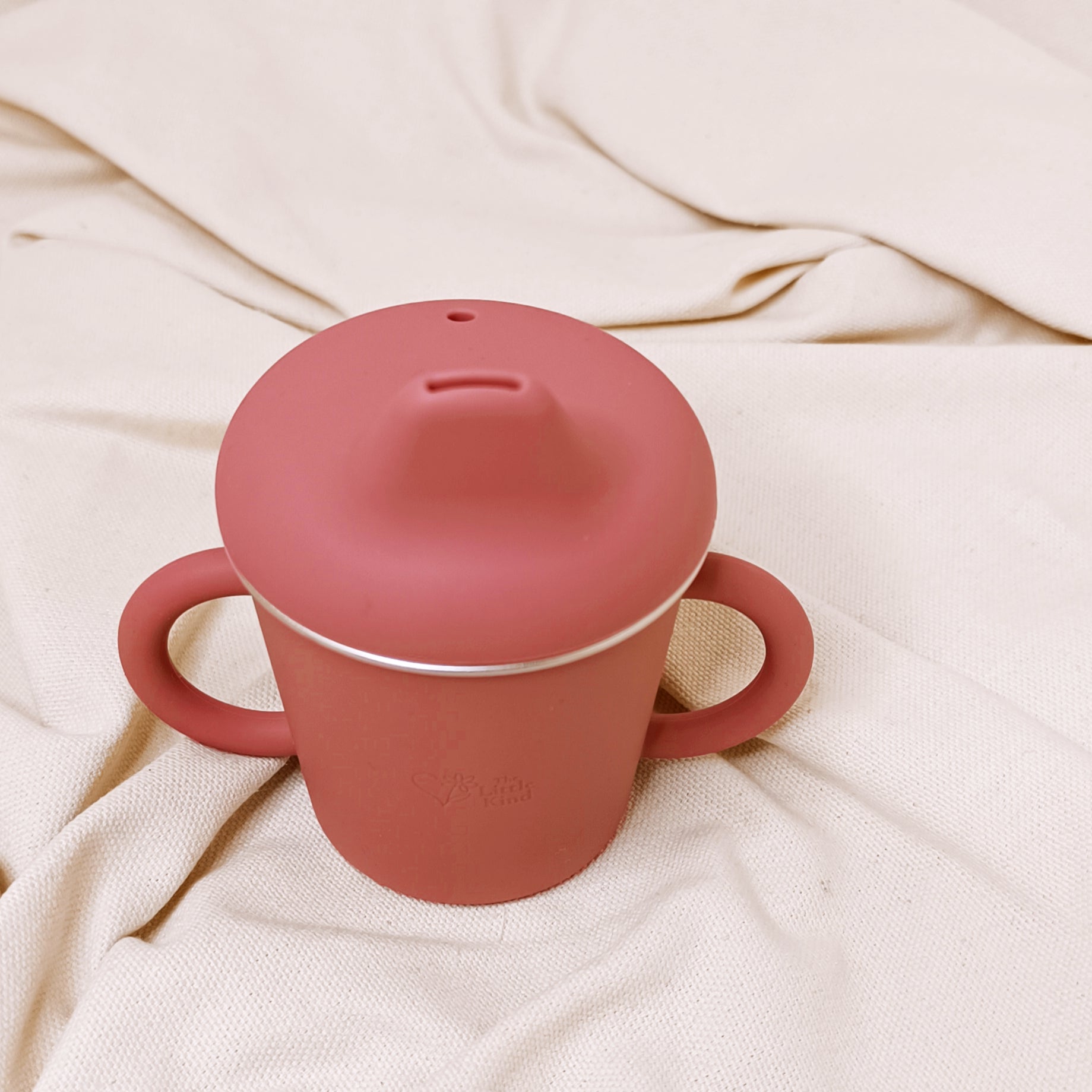 Pink sippy cup with a lid on a beige fabric background
