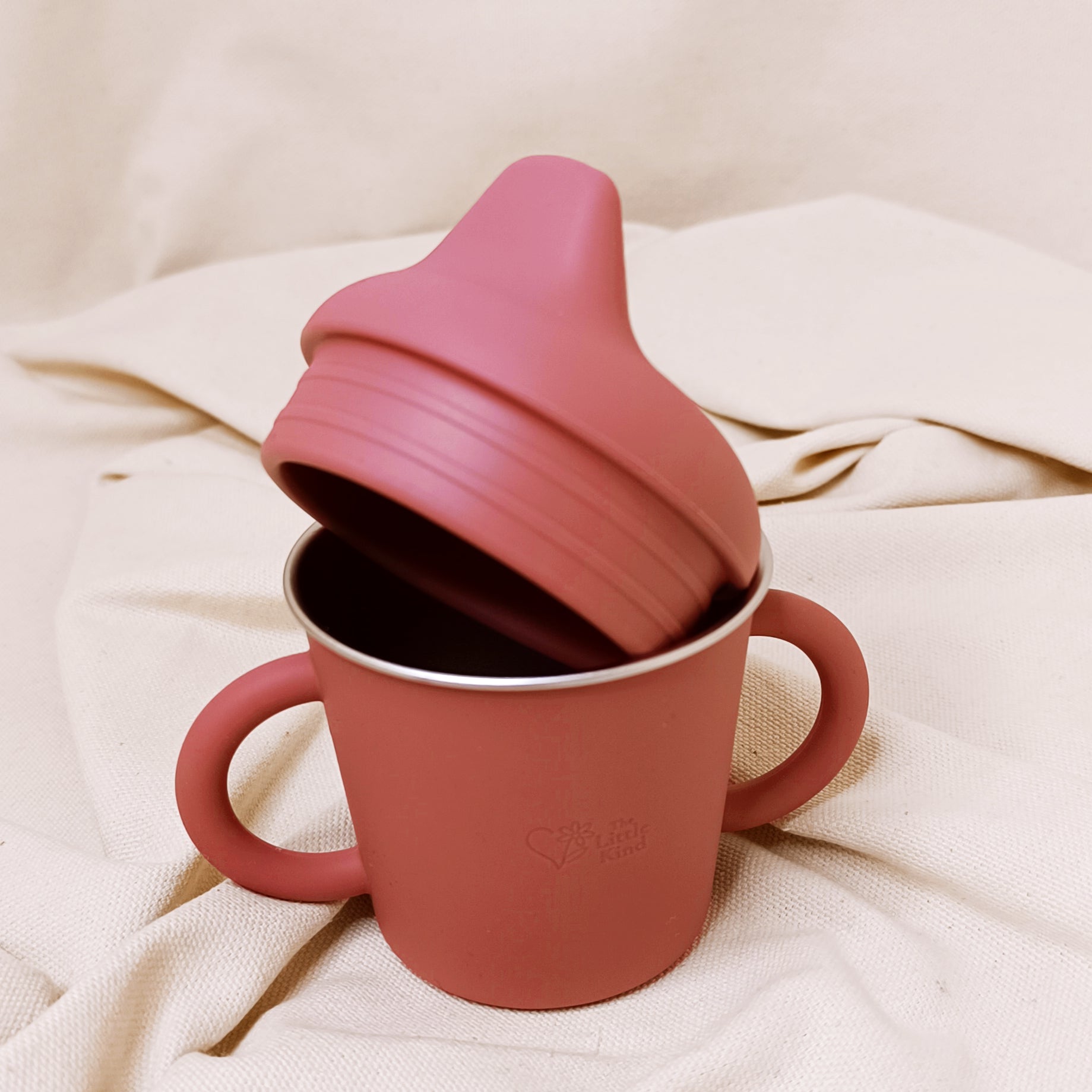 Pink sippy cup with a separate lid on a beige fabric background