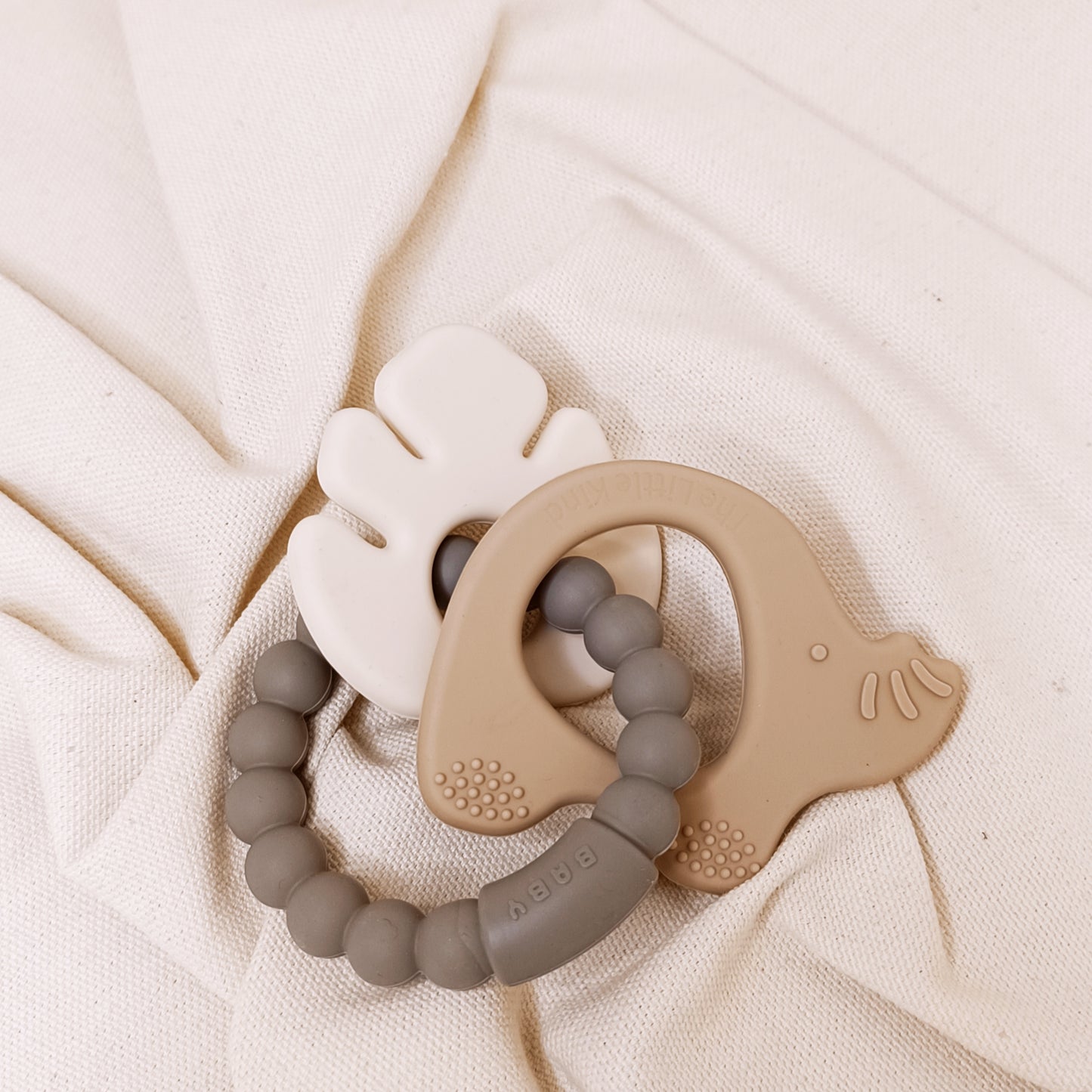 Two silicone teething rings on a soft beige fabric background