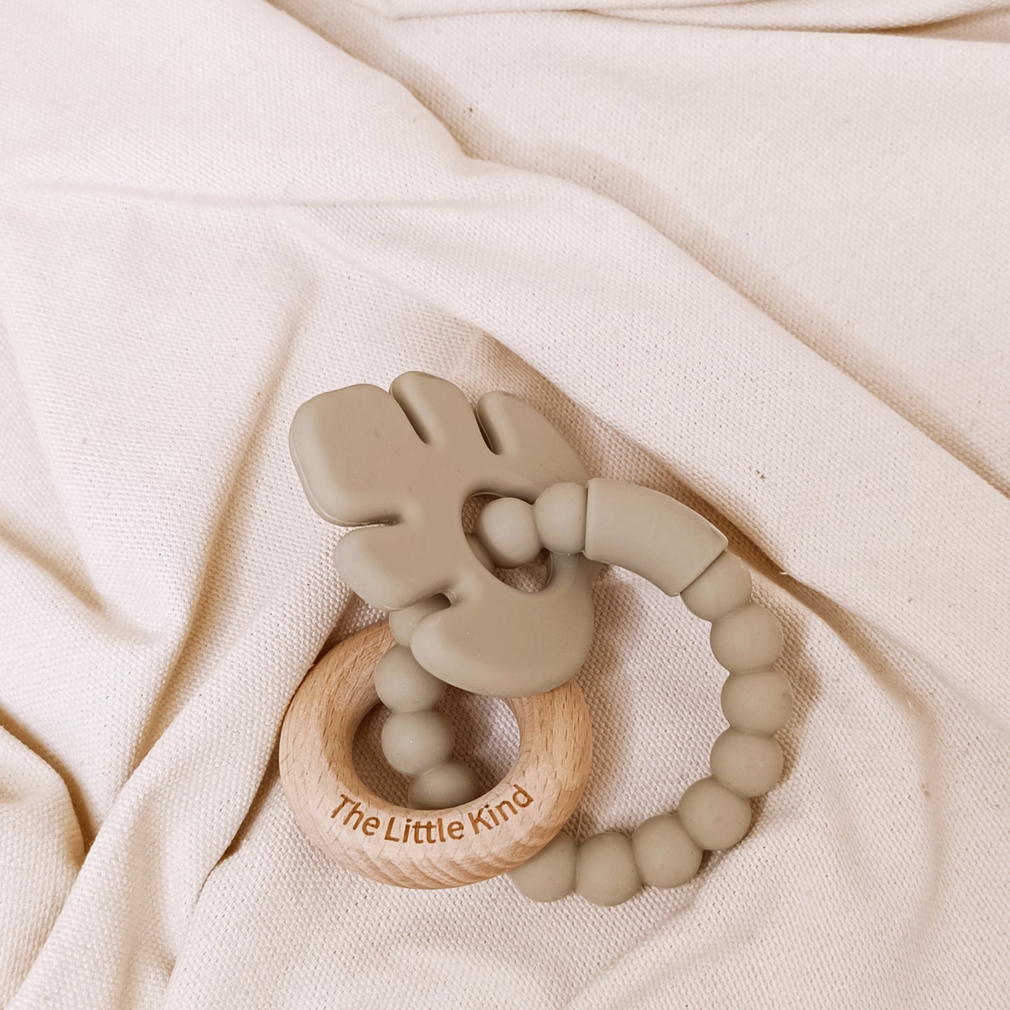 Teething ring with wooden base and silicone beads on a soft fabric background
