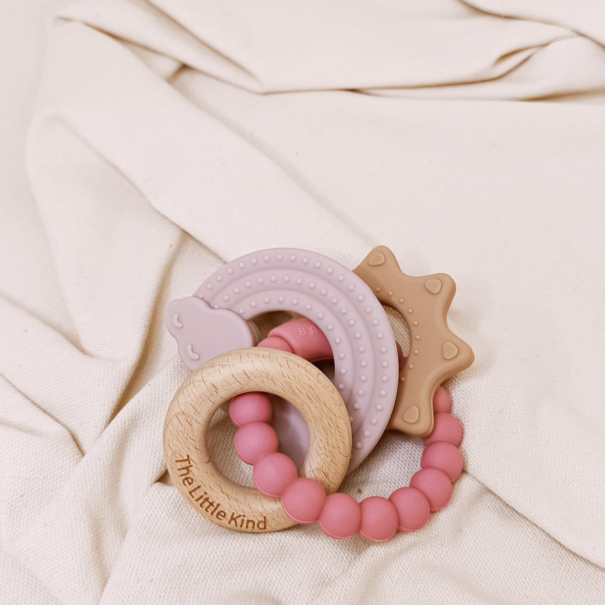 Three baby teething rings on a soft beige fabric background