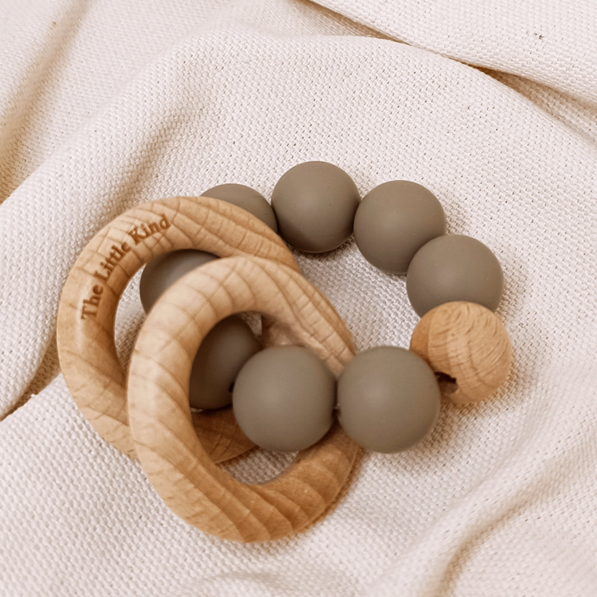 Teething ring with wooden and silicone beads on a beige fabric background