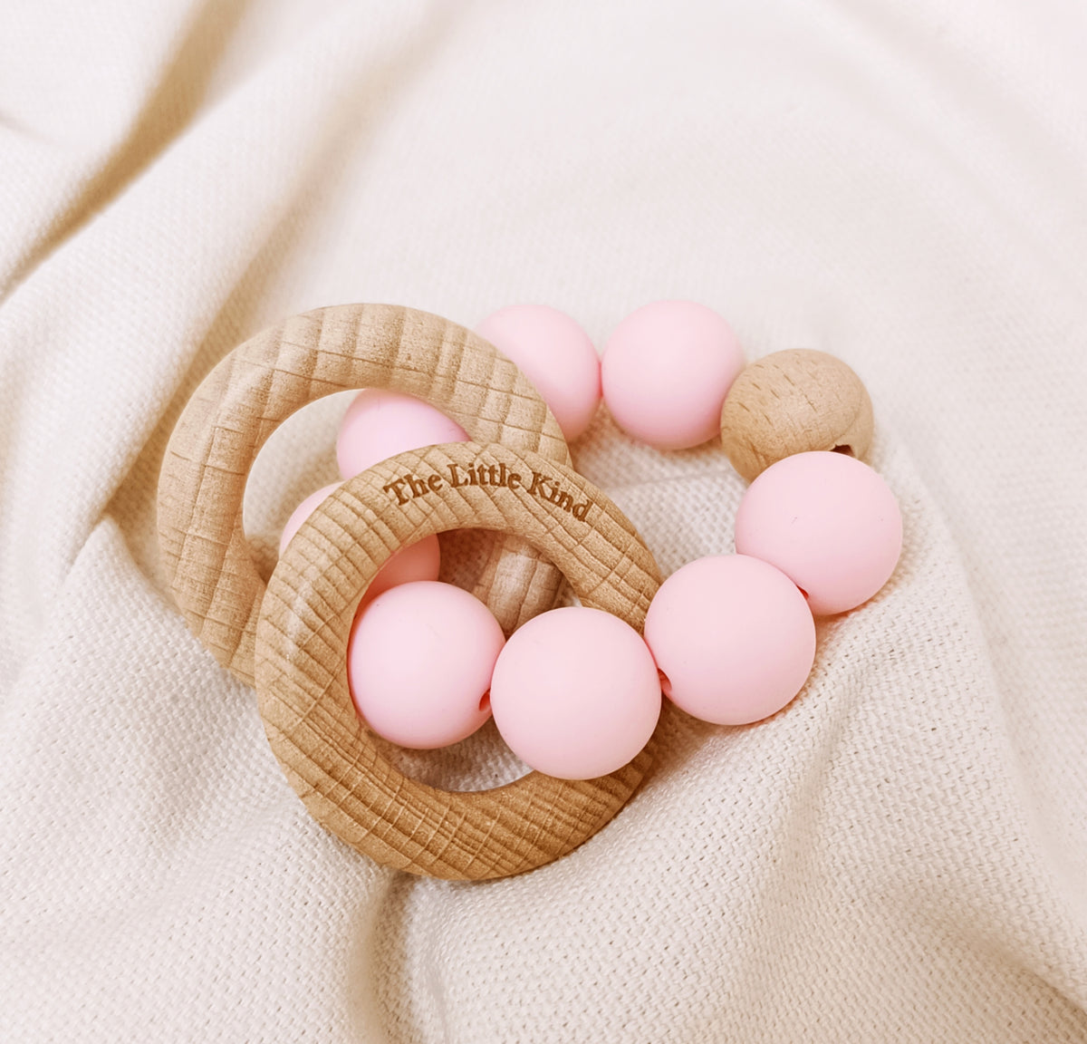 Teething ring with pink beads on a beige fabric background