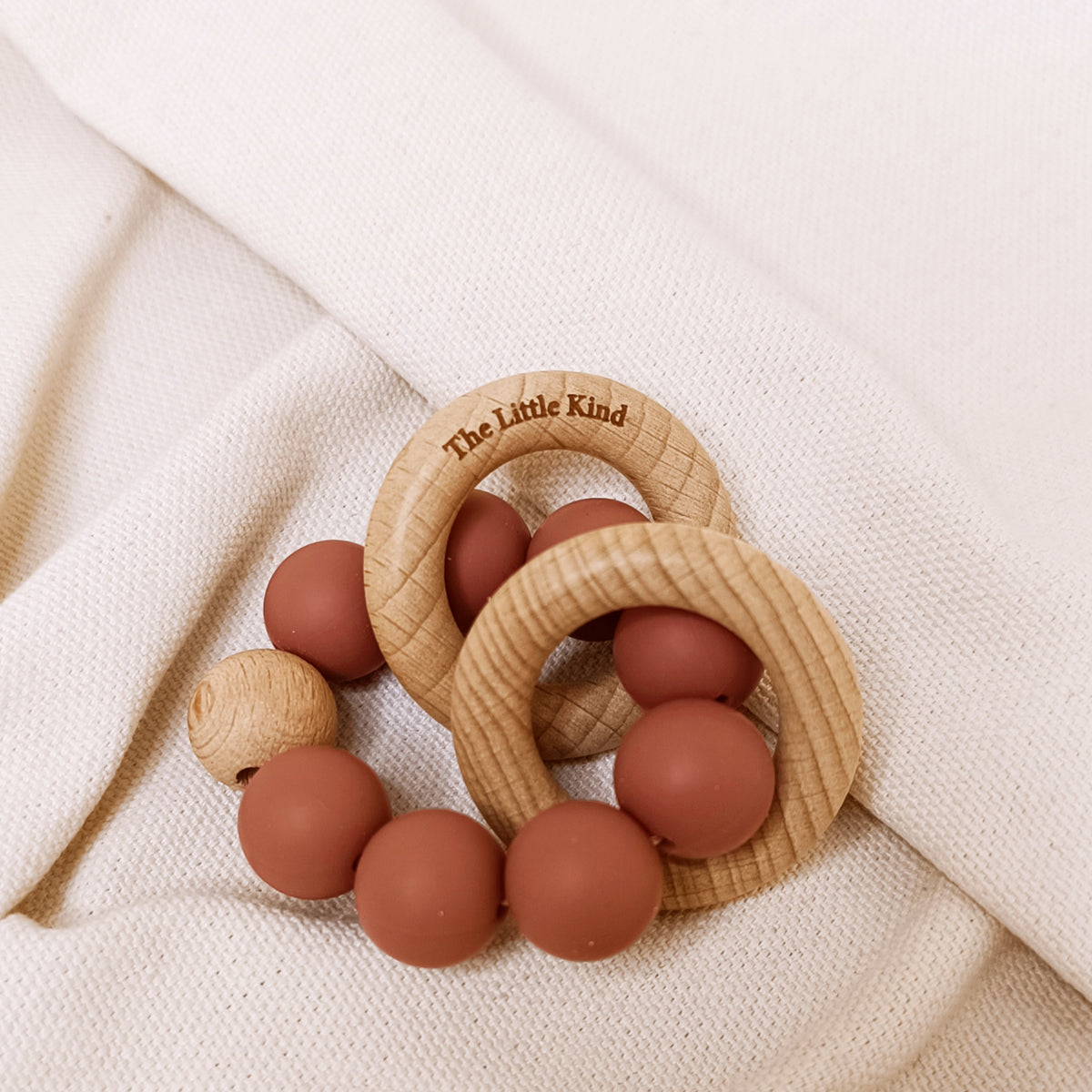 Wooden teething ring with pink beads on a beige fabric background